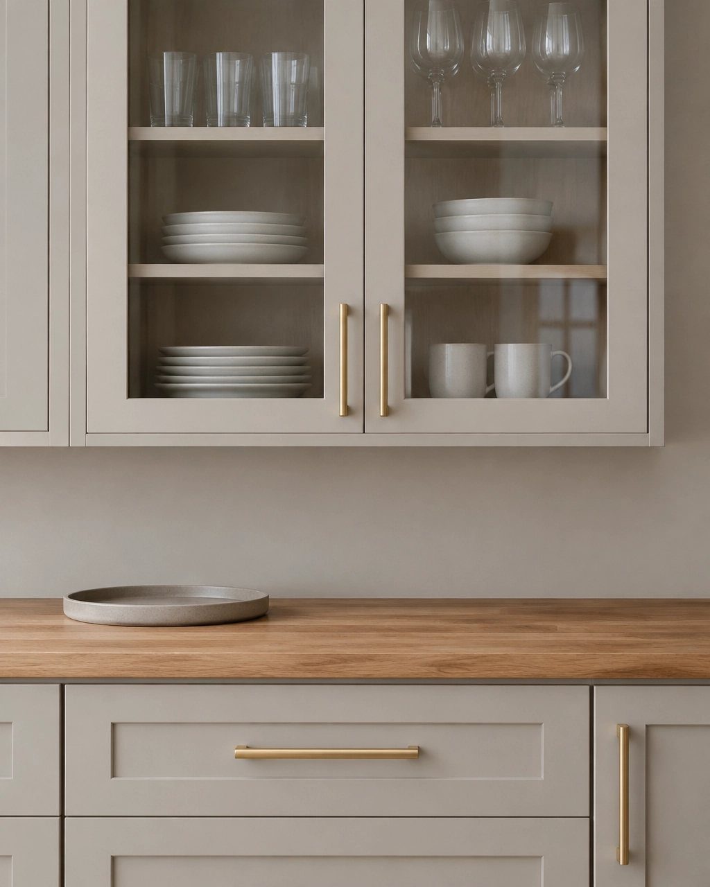 Grey kitchen cabinets with glass doors and gold hardware above a wood countertop