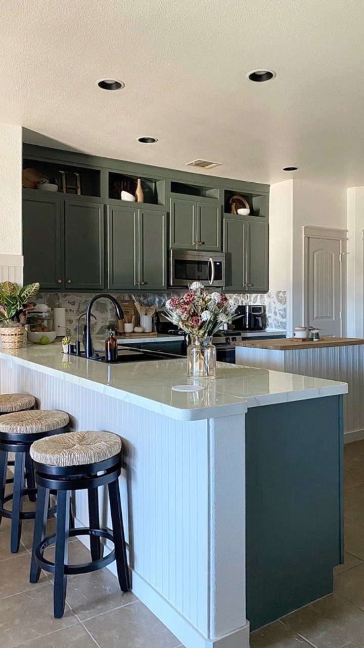 Dark green kitchen cabinets with open storage boxes added above the upper cabinets.