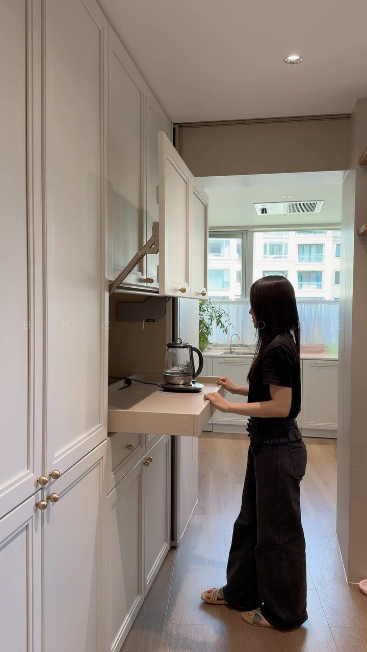 Woman using a vertical-raising cabinet system in a modern white kitchen.