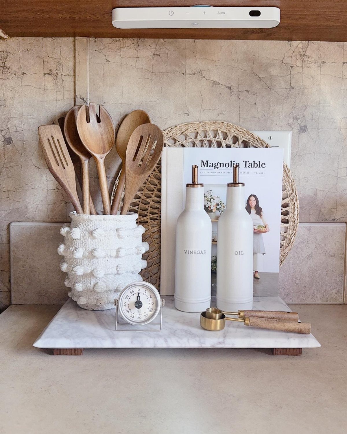 14 Kitchen Tabletop Decor Ideas to Style Your Counters 6 Marble tray holding wooden spoons in a crock, oil bottles, and a cookbook.