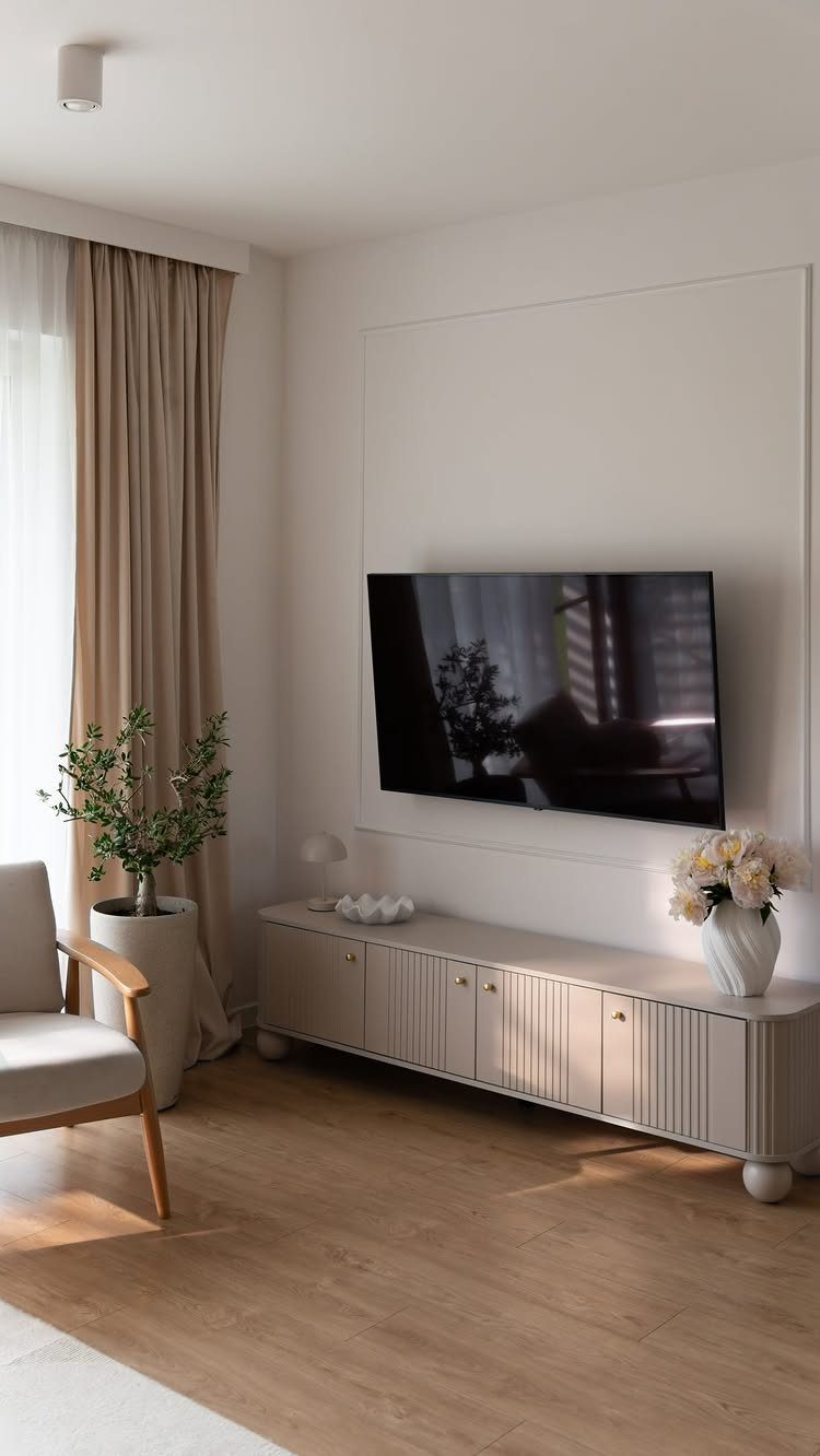 White low cabinet under a TV styled with a vase of flowers and bowl.