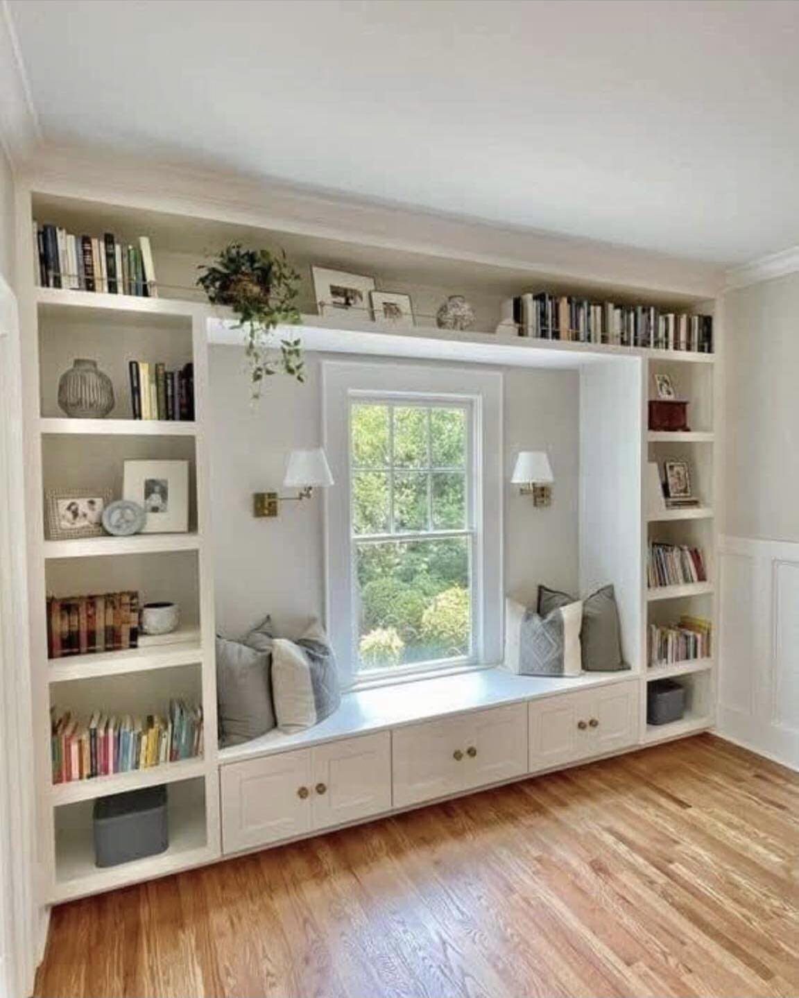White built-in window seat with storage drawers and surrounding bookshelves in a bright room.
