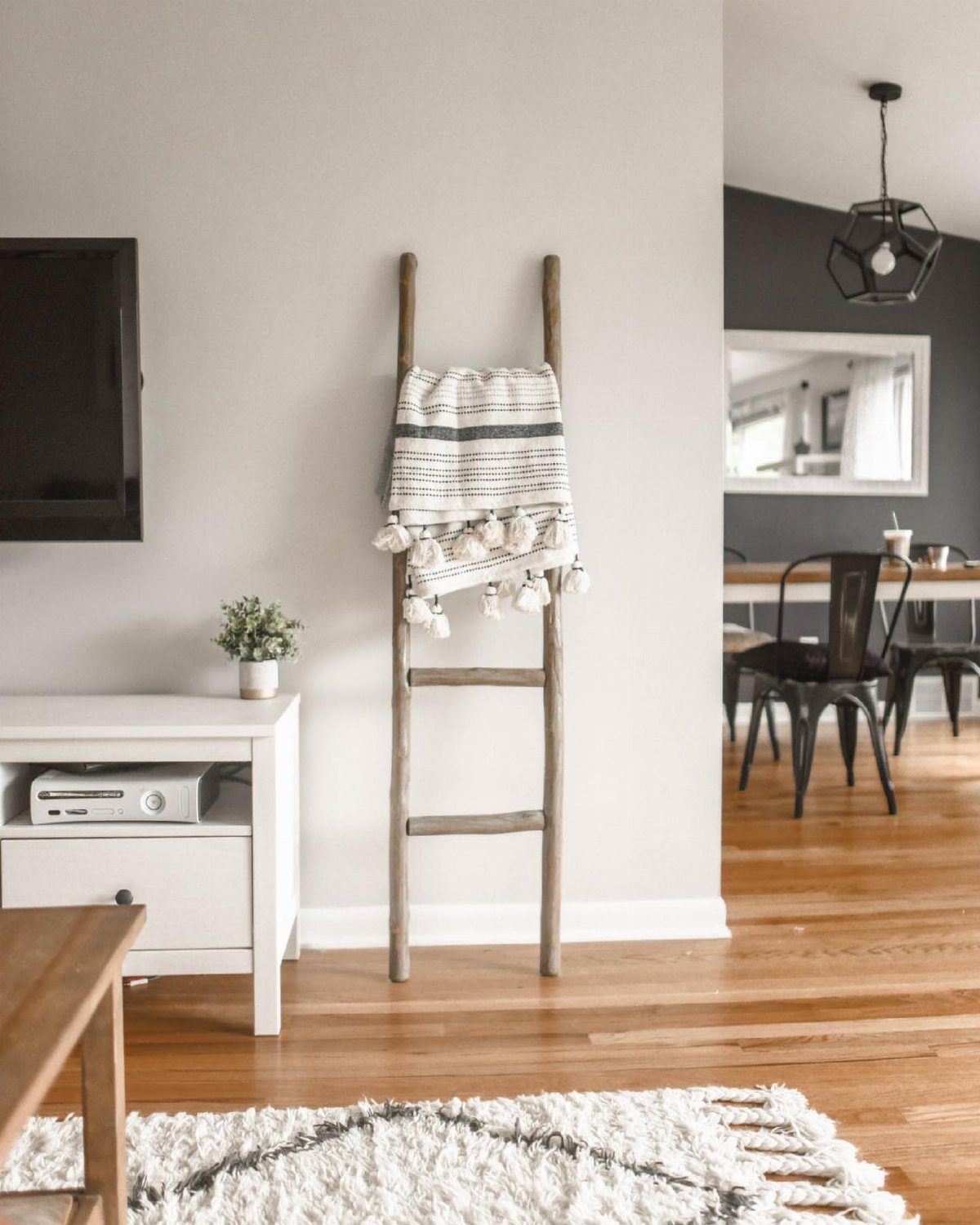 12 Modern Farmhouse Wall Decor Ideas for Living Room 12 Wooden decorative ladder leaning against a gray wall with a striped textile hanging.