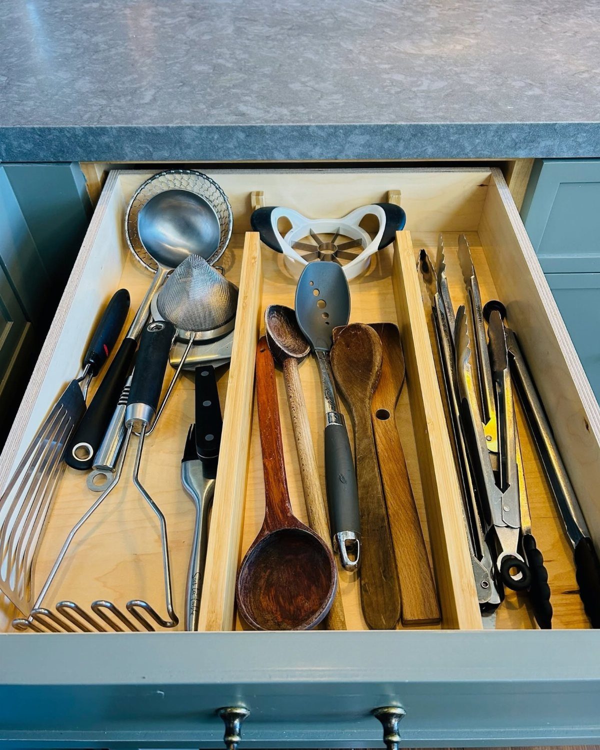 Kitchen drawer with wooden dividers organizing various metal and wooden cooking utensils.