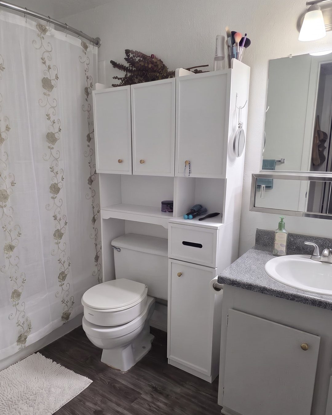 White wooden storage cabinet and shelving unit installed over a white bathroom toilet.