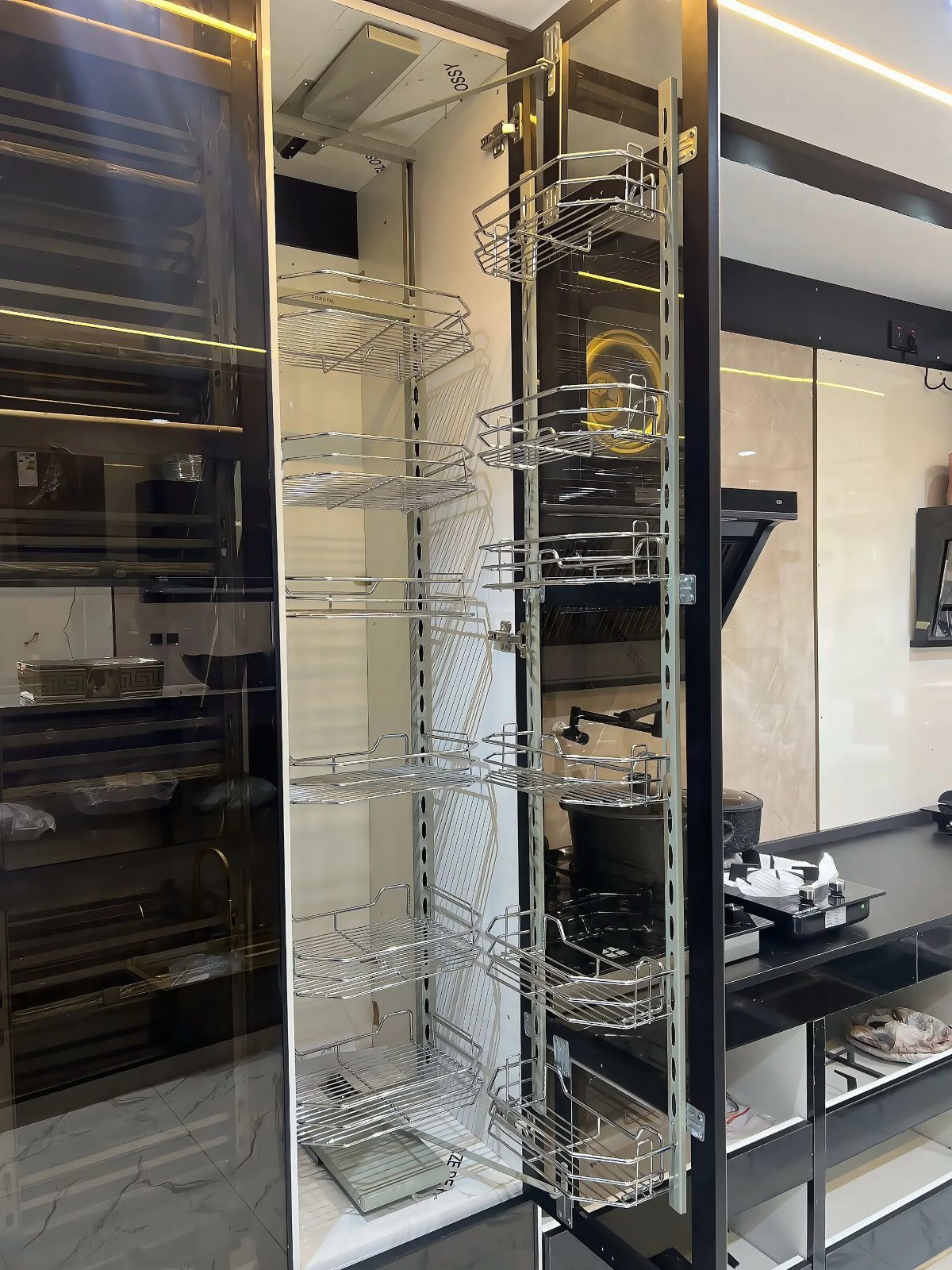 Pull-out pantry shelving with chrome wire baskets extended from a dark kitchen cabinet.