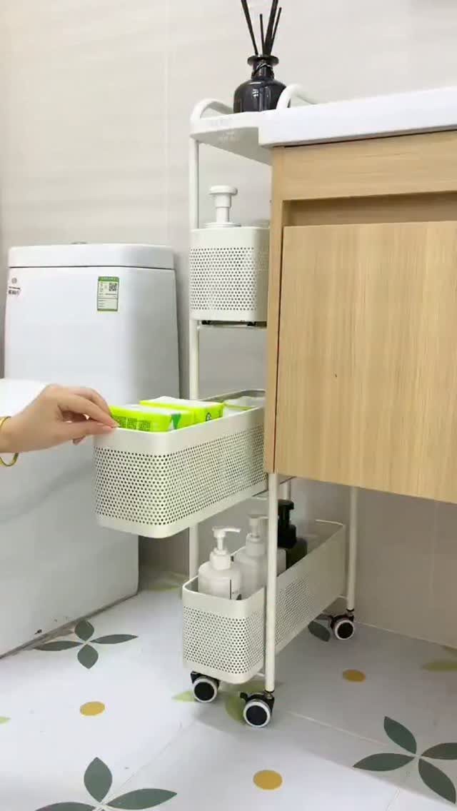 White rolling storage cart with perforated baskets next to a wooden cabinet.
