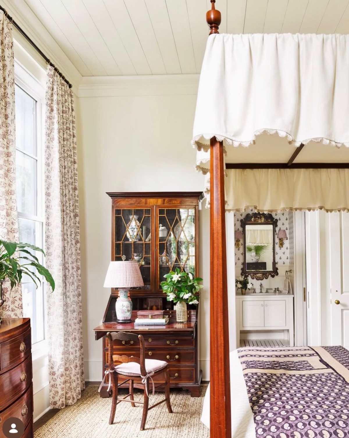 Antique wooden secretary desk with glass cabinets in a bright, traditional bedroom setting.
