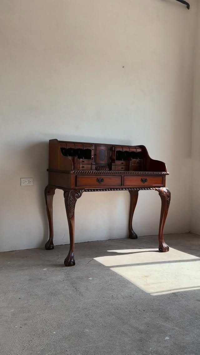 Vintage wooden secretary desk with cabriole legs against a white wall