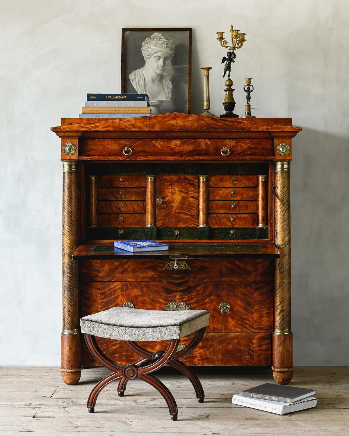 Empire style secretary desk with symmetrical columns and a small upholstered stool.