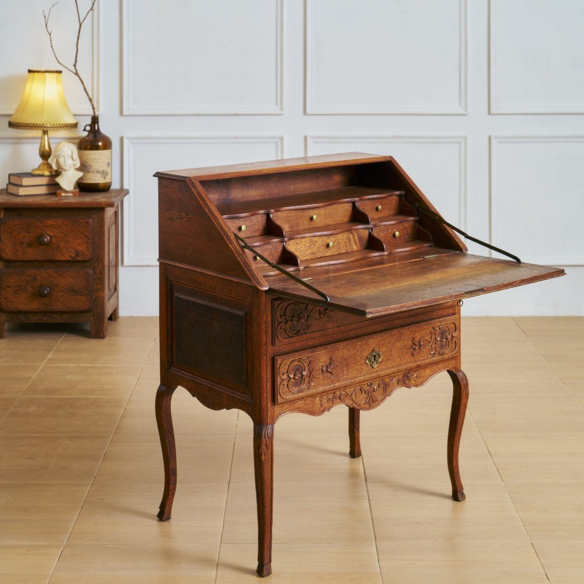 Vintage wooden secretary desk with slant-front and curved legs against a white wall.