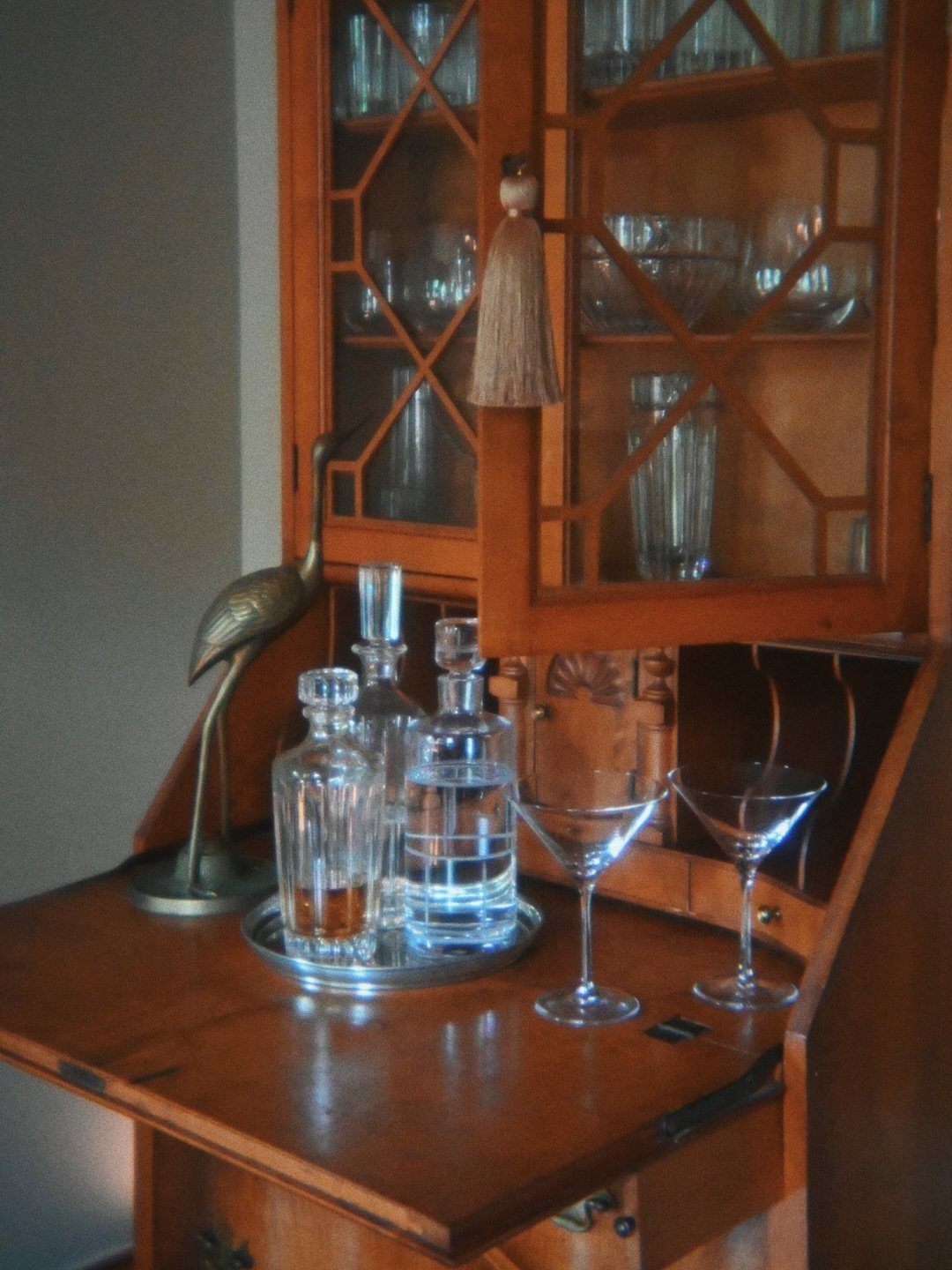 Wooden secretary desk used as a bar with glassware and decanters on the surface.