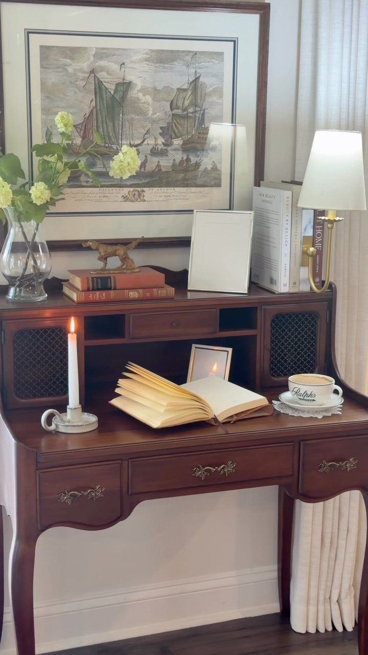 Antique dark wood secretary desk styled with a book, candle, and coffee in a room.