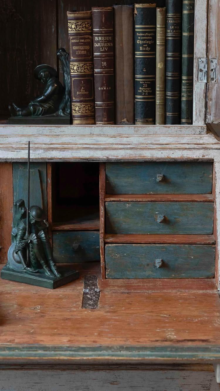 Antique slant-front secretary desk with teal drawers and old leather books inside.