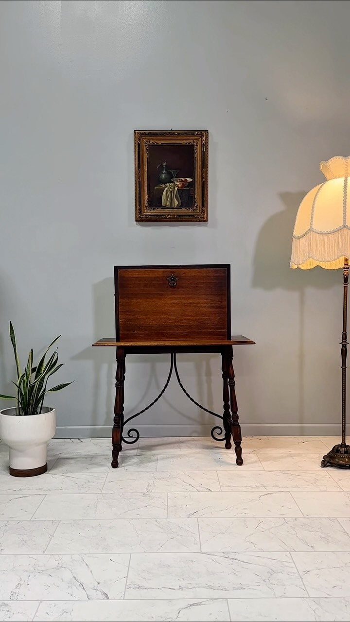 Vargueno desk with a drop-front surface and ornate legs against a grey wall.