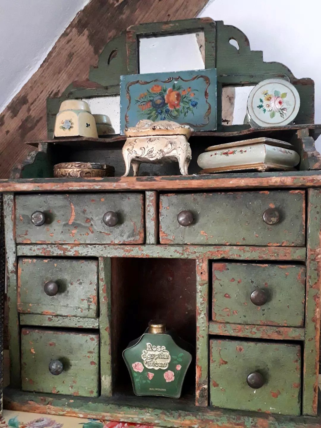 Green vintage wooden cabinet with a chippy painted finish and small decorative items.