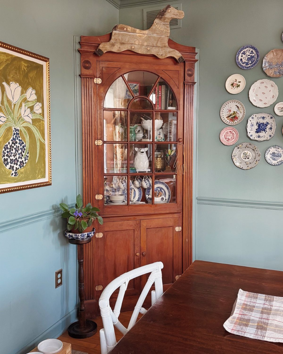 Wooden corner hutch with glass doors and a carved horse on top.