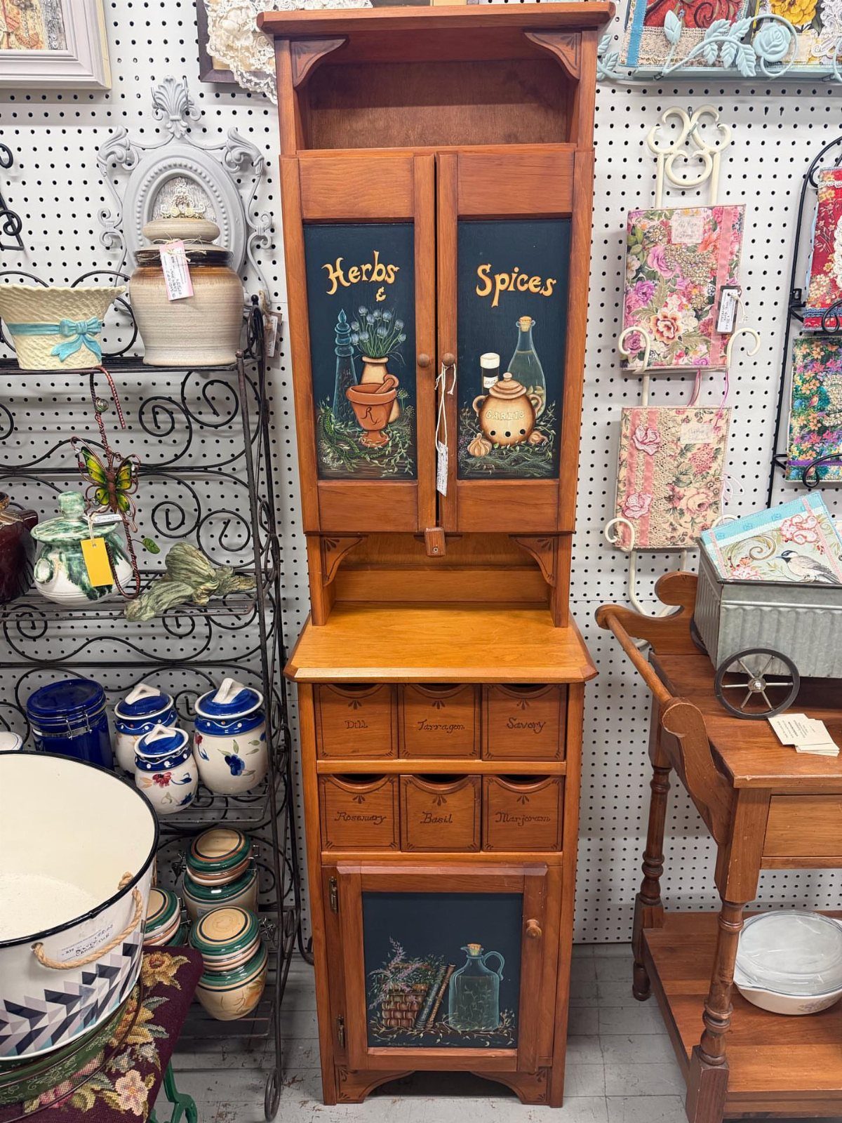 Wooden hutch with painted herb and spice panels and small labeled spice drawers.
