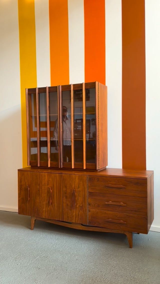 Mid-century modern wood hutch with drawers and cupboards against a striped wall.