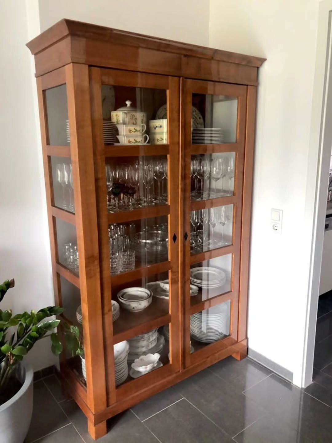 Natural wood hutch with glass doors displaying clear glassware and white ceramic dishes.
