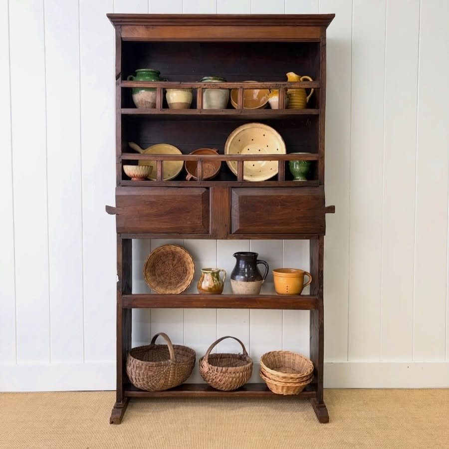 Dark brown wooden hutch with open shelves holding ceramics and woven baskets.