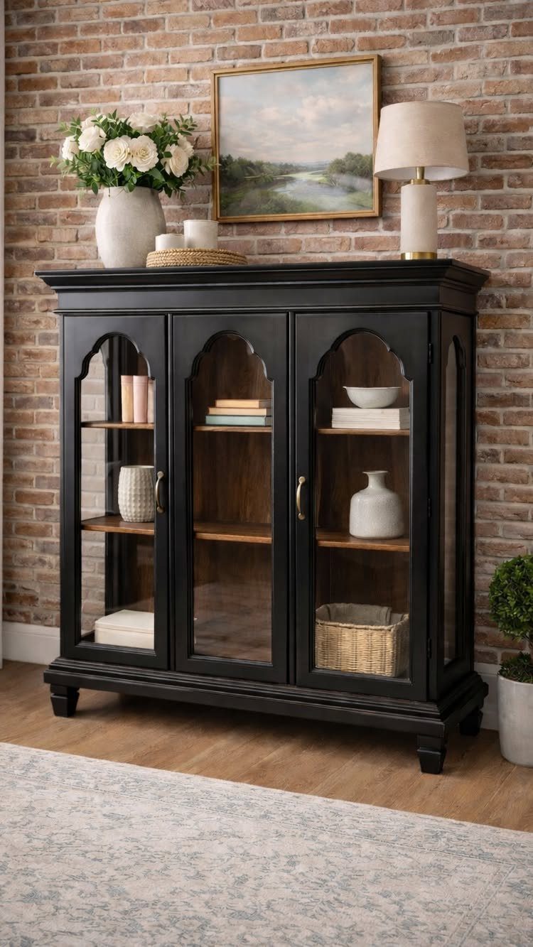 Black painted wood hutch with arched glass doors against a brick wall