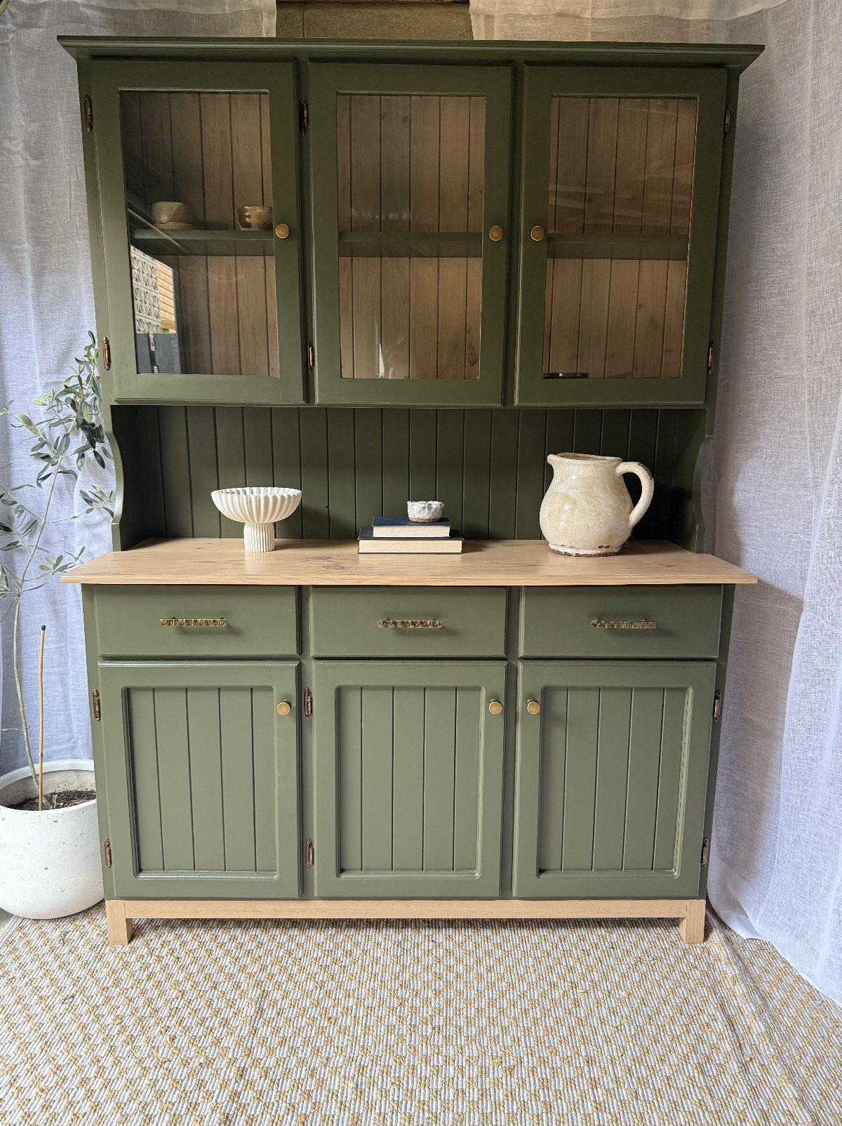 Sage green painted wooden hutch with glass upper cabinets and natural wood countertop.