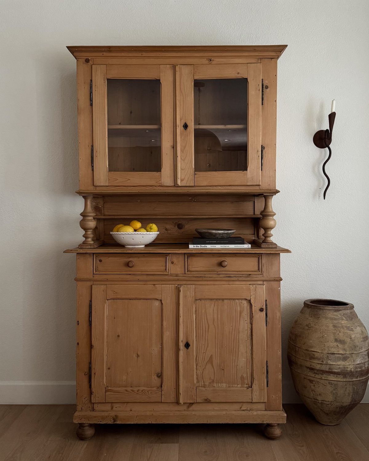 Antique wooden hutch with glass upper cabinets and lower cupboards against a white wall.