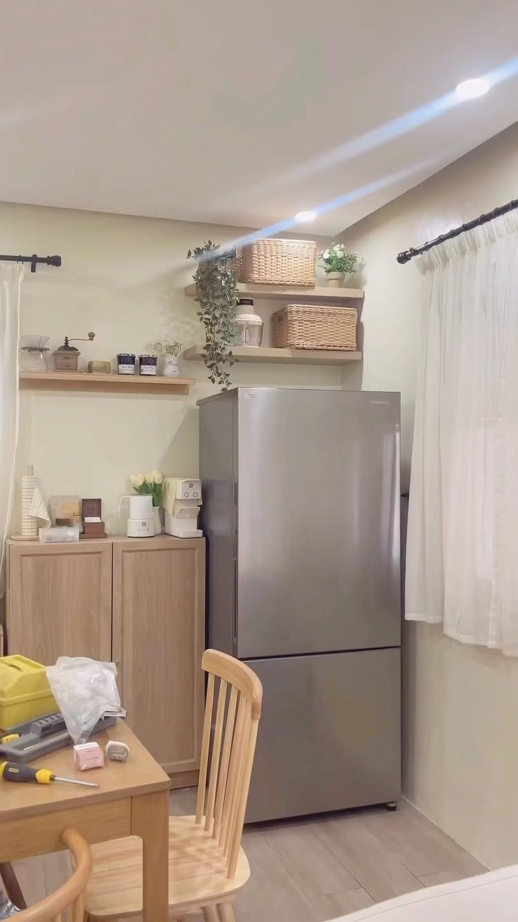 Silver refrigerator with light-wood floating shelves holding woven baskets and plants above it.