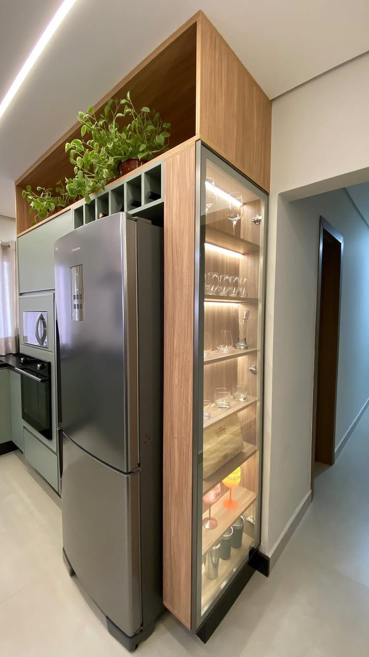 Glass-front cabinet with interior lighting displaying glassware next to a stainless steel refrigerator.