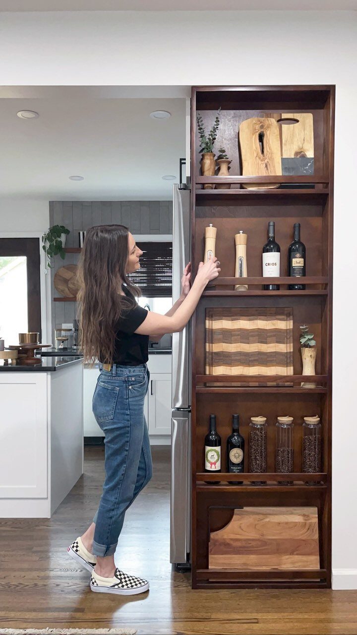Woman standing next to a tall dark wood shelving unit beside a refrigerator
