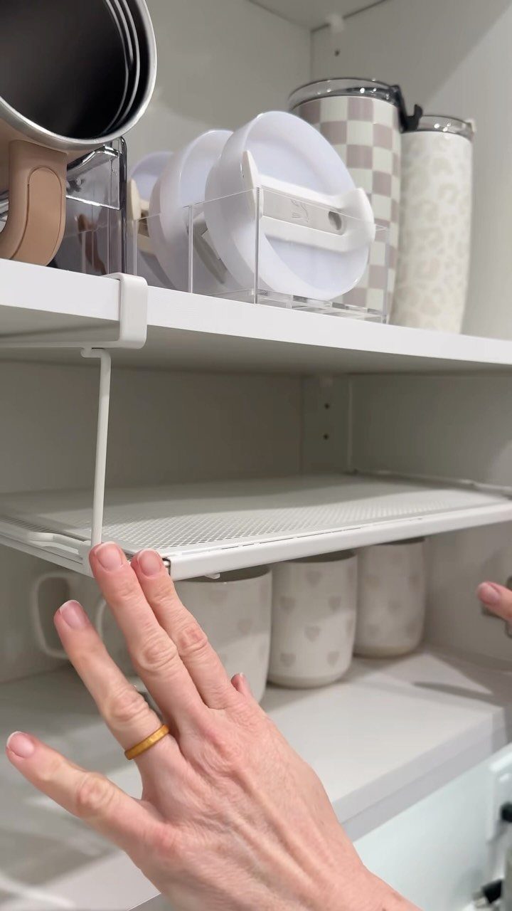 White under-shelf storage basket being pulled out from a white kitchen cabinet shelf.