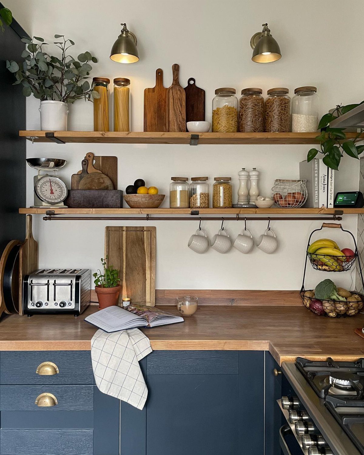 19 Small Kitchen Reno Ideas That Maximize Every Inch 3 Wooden floating shelves with kitchen jars and cutting boards above blue cabinets.