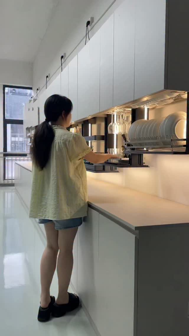 19 Small Kitchen Reno Ideas That Maximize Every Inch 18 Woman using a pull-down cabinet organizer for plates in a white modern kitchen.
