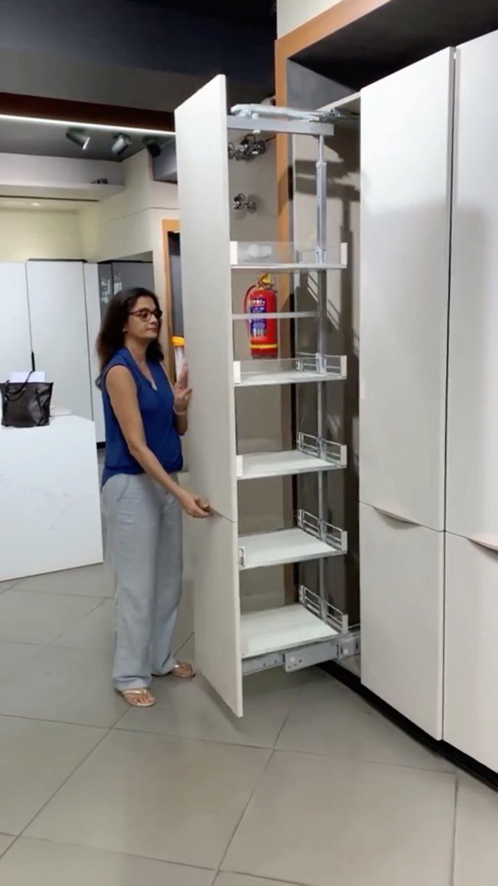 19 Small Kitchen Reno Ideas That Maximize Every Inch 8 Woman standing next to a tall white pull-out pantry cabinet with multiple shelves.