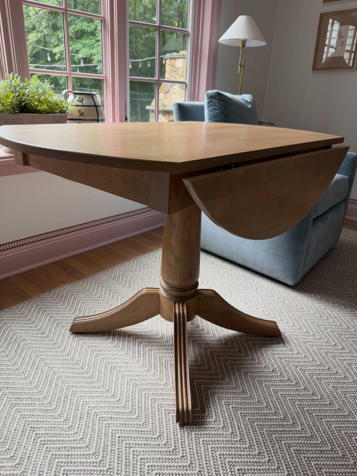 Wooden drop leaf table with one side folded down on a chevron rug.