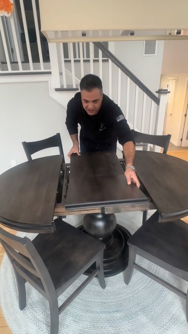 Dark brown wooden expandable dining table with a man demonstrating the leaf insert.