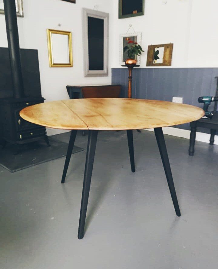 Round wooden extendable table with black legs in a room with grey walls.