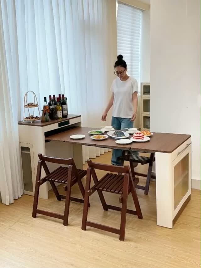 Pullout dining table extended from a white cabinet with two brown folding chairs.