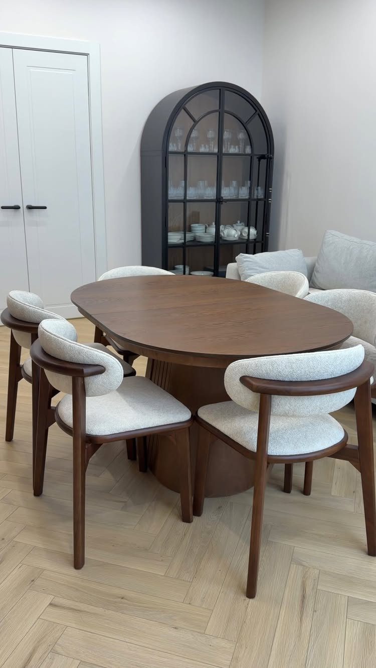 Round brown wooden dining table with white upholstered chairs on herringbone wood flooring.