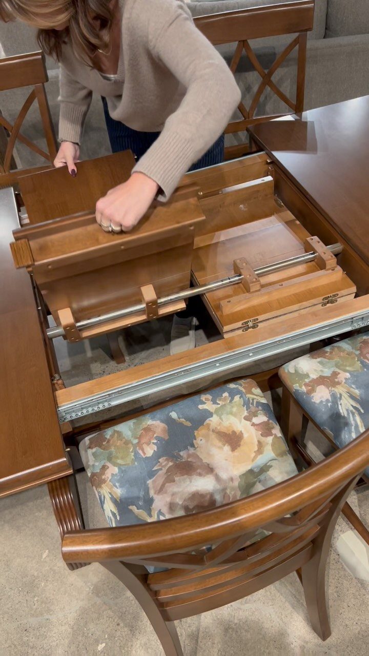 Wooden dining table with a butterfly leaf being unfolded by a person's hands.