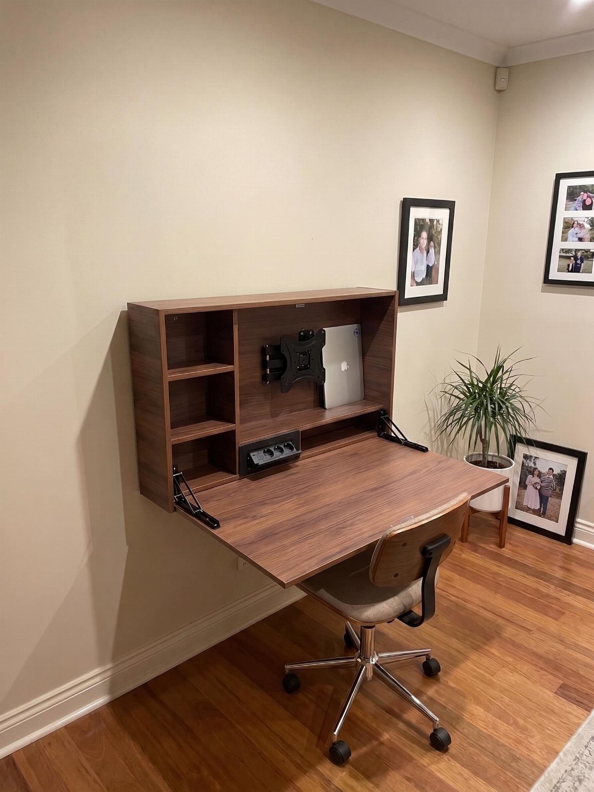 Wall-mounted folding brown wood desk with hutch and white office chair in room.
