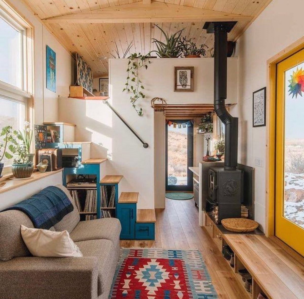 Tiny House Layout Ideas: 27 Smart Ways to Maximize Space 19 Tiny house interior with a grey sofa, wood stove, and blue built-in storage.