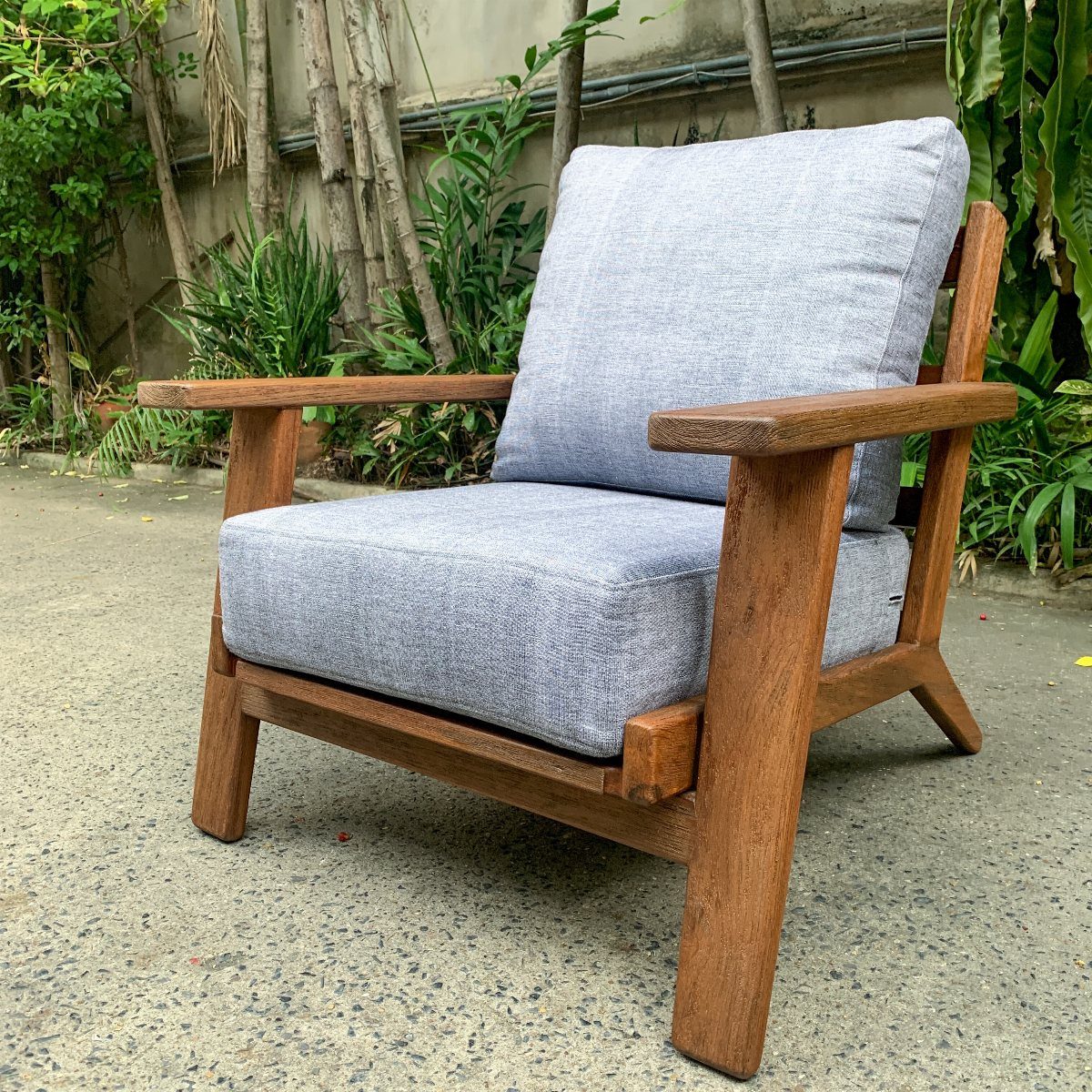 Wood Lounge Chair Ideas: 28 Styles from Teak to Mid-Century 5 Wooden lounge chair with thick gray cushions set against a lush green garden background.